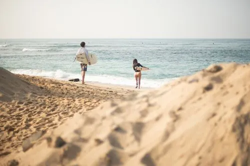 Two people walking on the beach with surfboards.