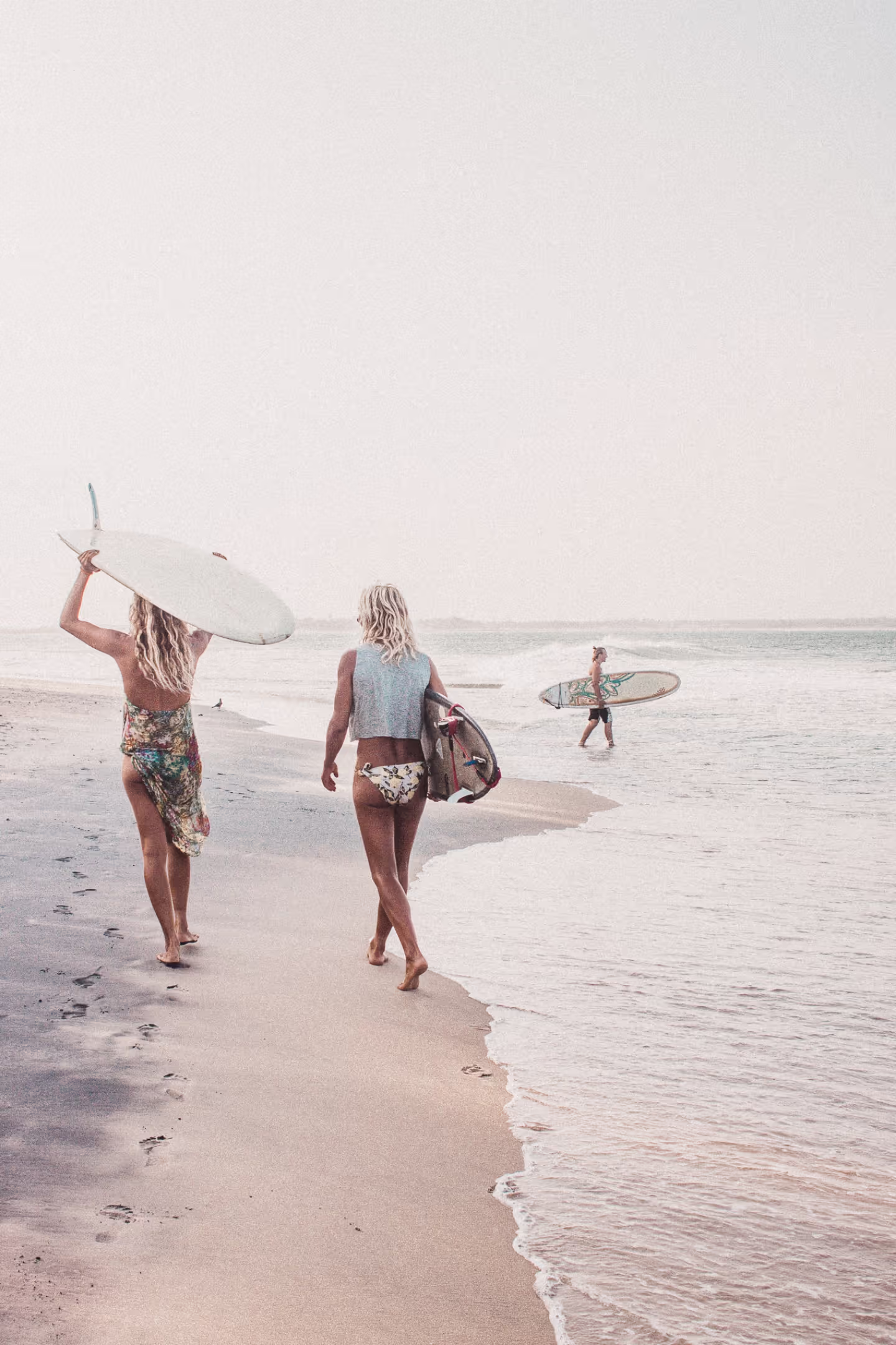 Two women walking on the beach with surfboards.
