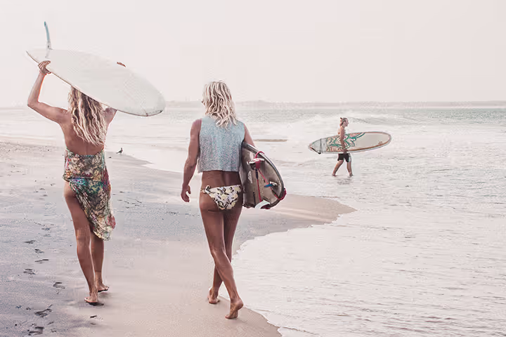 Two women walking on the beach with surfboards.