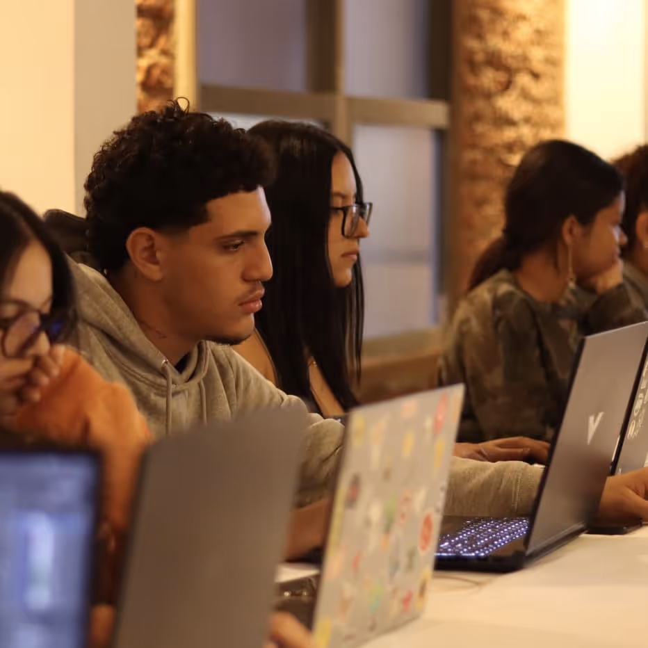 Young adults focused on working on their laptops in a casual indoor setting.