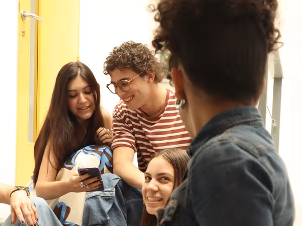 Group of four young people sitting together, smiling and looking at a phone.