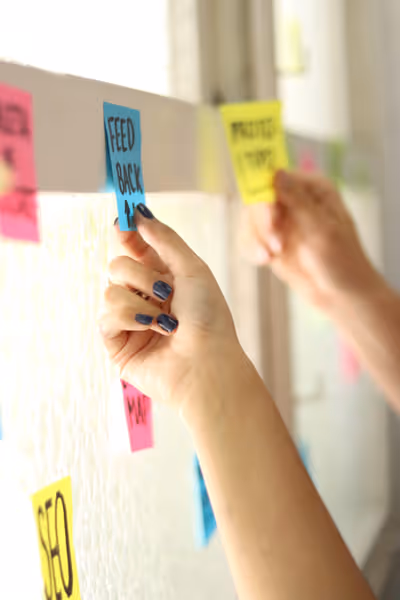 Hands placing colorful sticky notes labeled with business terms like 'FEEDBACK' on a glass surface.