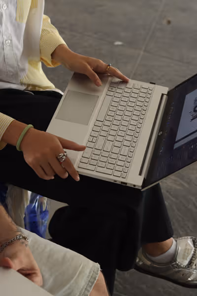 Person wearing rings and a green bracelet using a beige laptop while sitting on a gray floor.