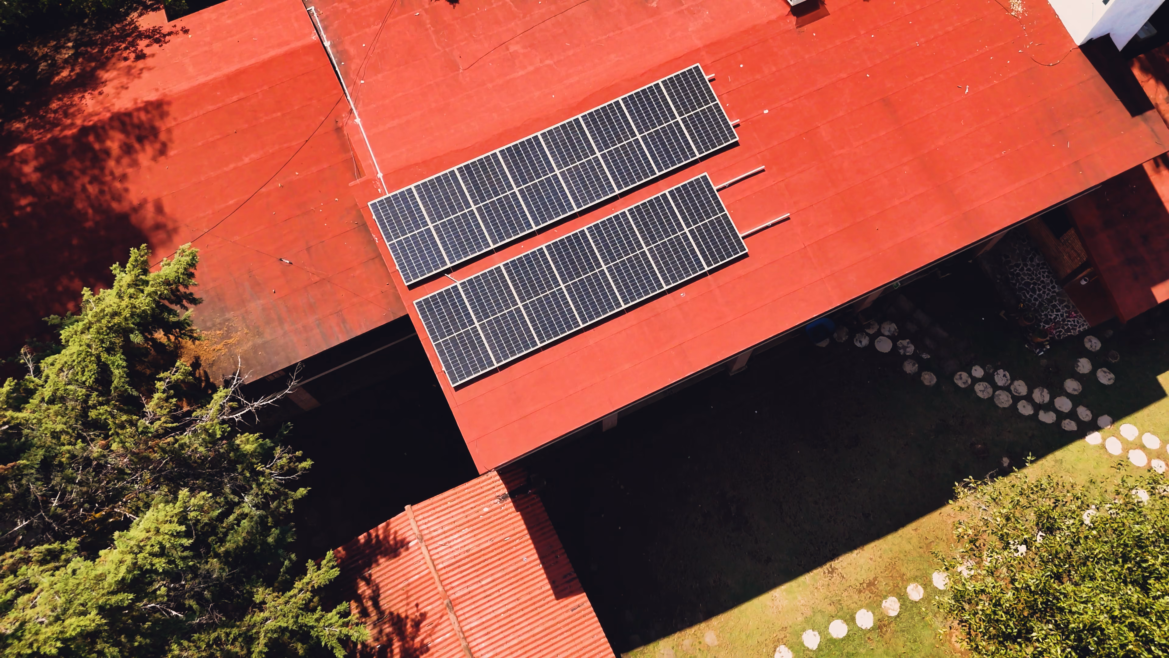 Paneles solares instalados en el techo rojo de una casa con árboles y jardín alrededor.