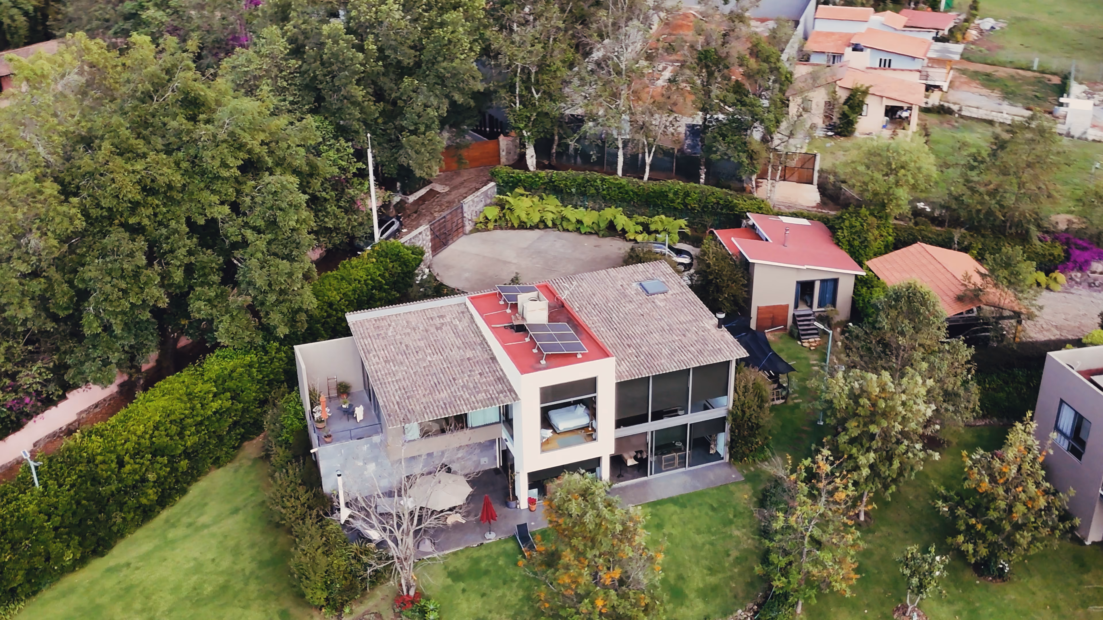 Casa moderna de dos pisos con paneles solares en el techo, rodeada de árboles y jardines verdes.