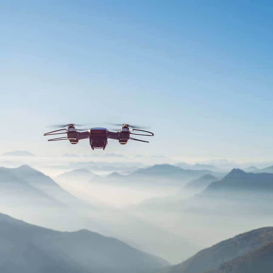 Drone flying over misty mountain ranges under clear blue sky.