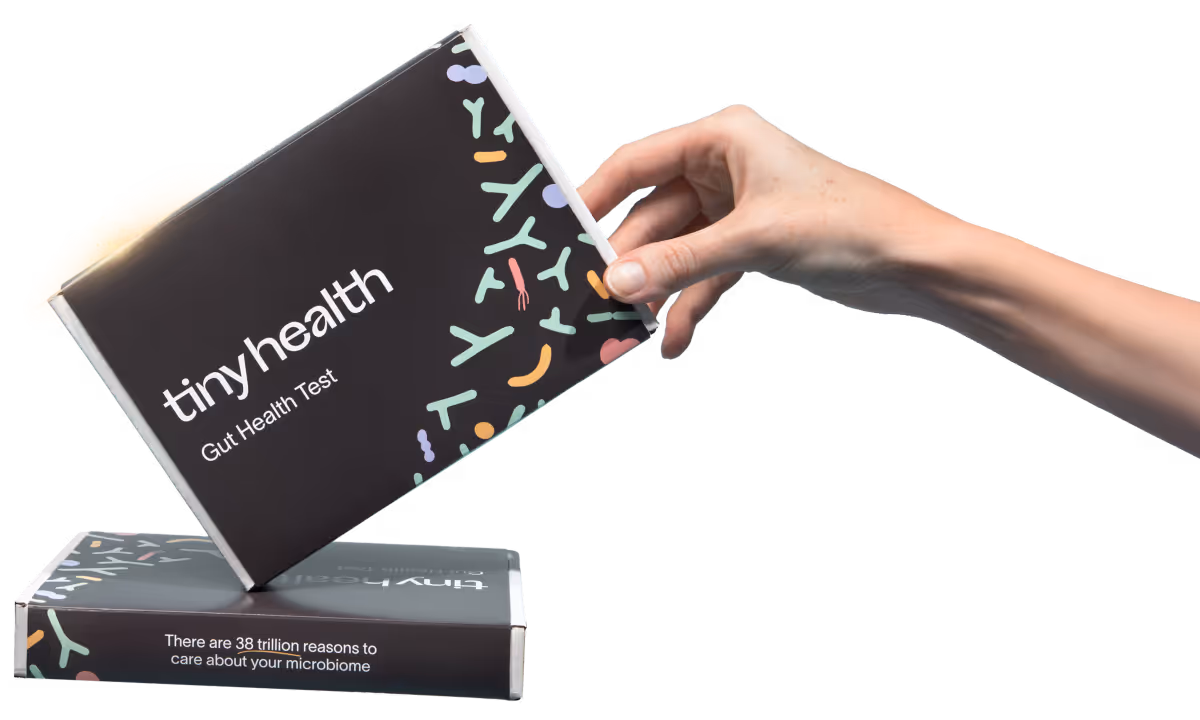 Hand holding a Tiny Health Gut Health Test box above another box with text about microbiome importance.