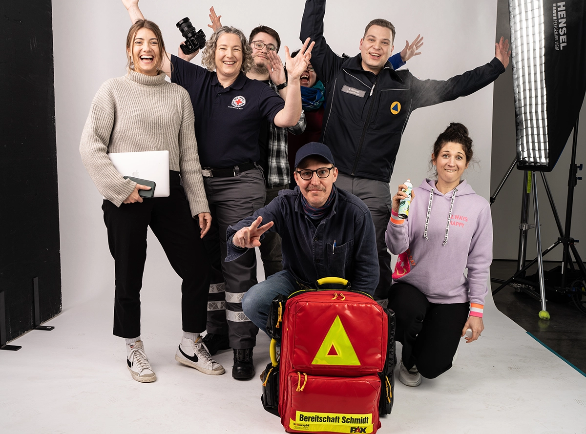 Ein Gruppenbild mit sieben glücklichen Personen, die in die Kamera strahlen, stehen vor einer Hohlkehle eines Fotostudios.