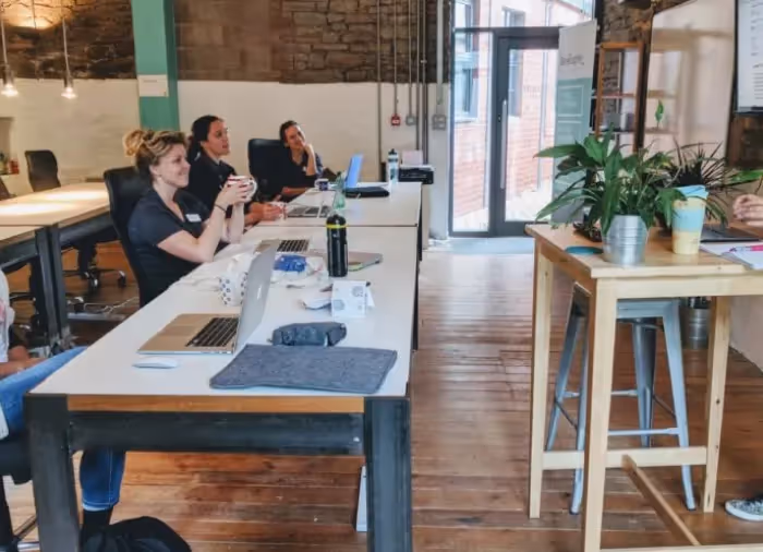 A picture of the DevelopMe offices with a speaker at the front of the room and people sitting at desks listening. 
