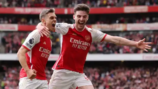 Arsenal football players celebrating a goal during a match at the Emirates Stadium, wearing red and white home kits.