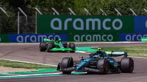 Aston Martin Formula 1 car leading another car through a corner during a race, with Aramco sponsorship banners in the background.