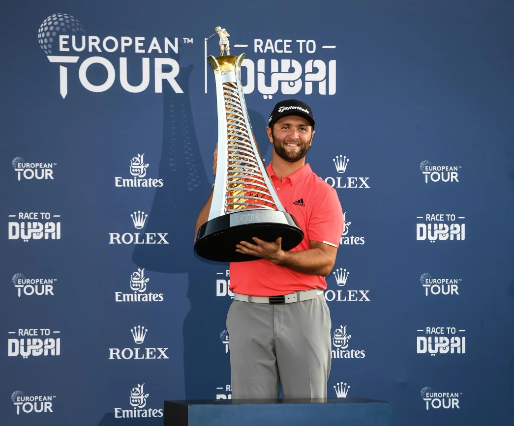 Professional golfer celebrating victory by holding a large trophy on stage at a European Tour event, with prominent branding and backdrop illustrating the impact of sports sponsorship in international golf. The scene highlights the connection between athletes, major tournaments, and sponsor partnerships.