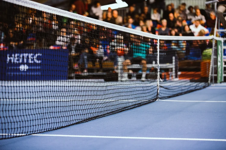 Indoor tennis court with close-up of the net and event sponsorship banners in the background, highlighting brand visibility and audience engagement at sports events.