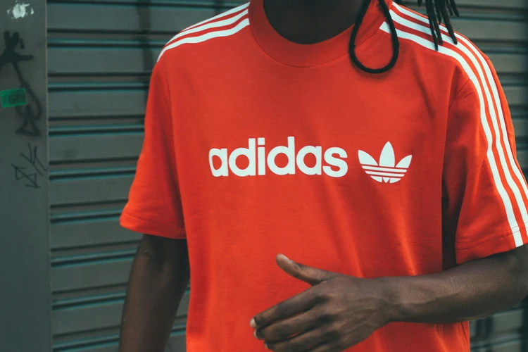 Close-up of a person wearing a red Adidas t-shirt with prominent white logo and stripes, showcasing iconic sports branding and brand visibility in athletic apparel.