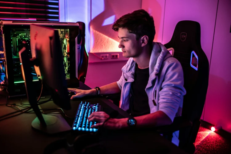 Young male gamer at RGB-lit PC setup in modern gaming chair, focused on esports competition, representing esports sports sponsorships in a professional environment.