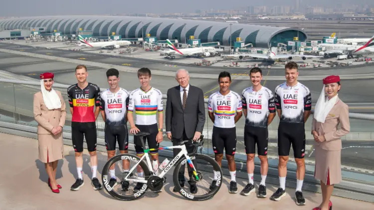 Emirates Airline executives and UAE Team Emirates XRG cyclists at Dubai Airport, showcasing sports branding through team uniforms and corporate partnership.