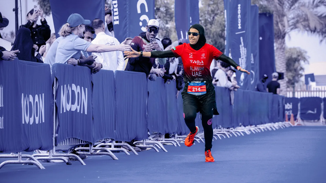 UAE triathlete in a TAQA race suit high-fives fans beside Modon branded barriers at WTCS Abu Dhabi, a sports sponsorship showcase