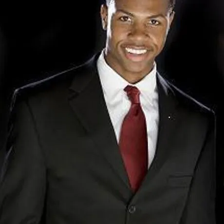 Smiling professional in black suit and red tie against dark background