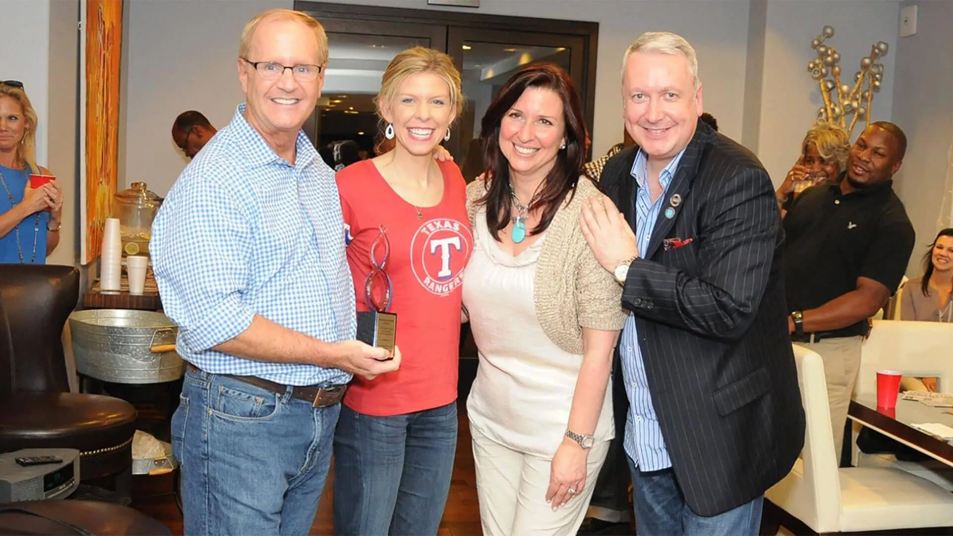 Four smiling people at casual event, woman wearing Texas Rangers shirt