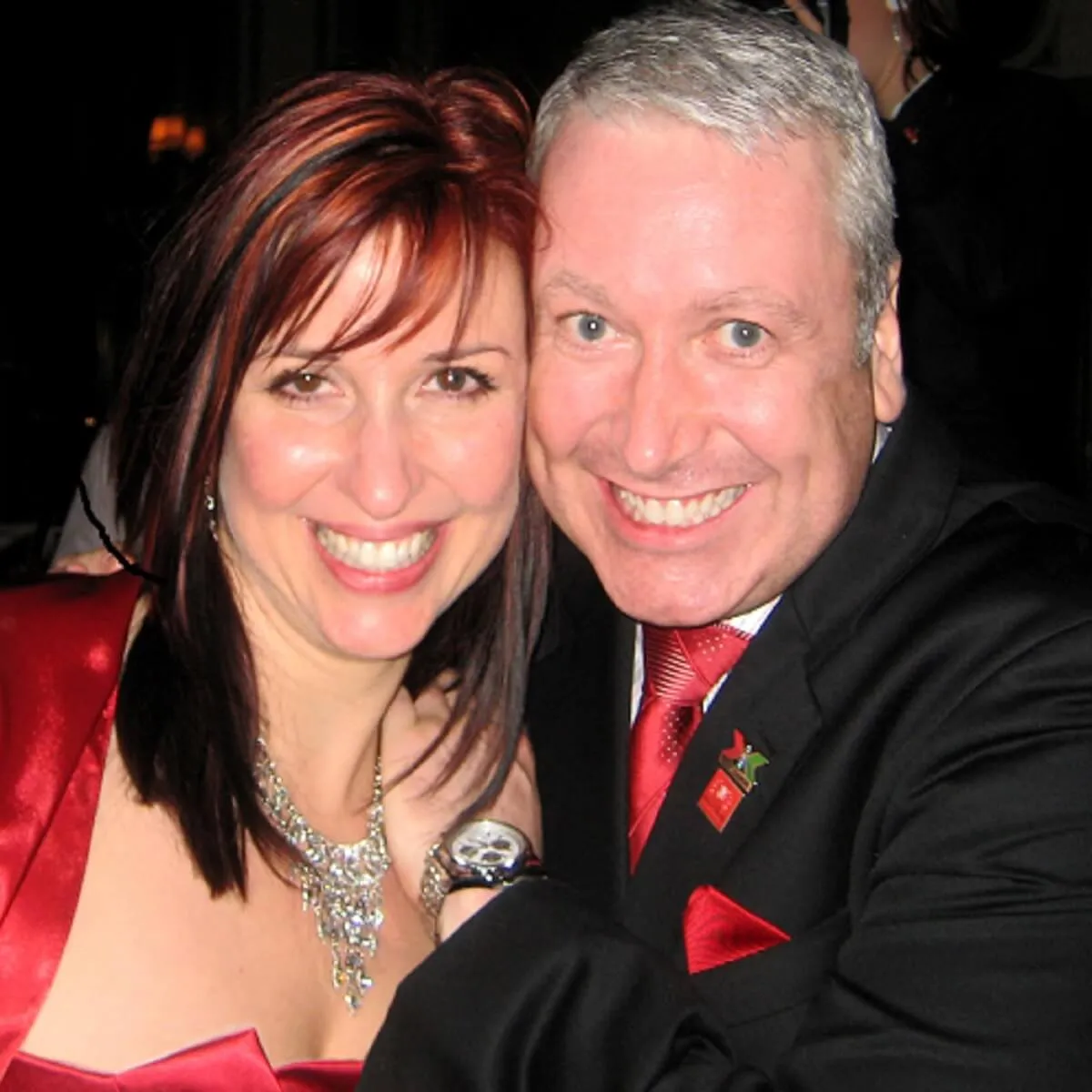 Two people smiling together at a formal event, wearing red and black