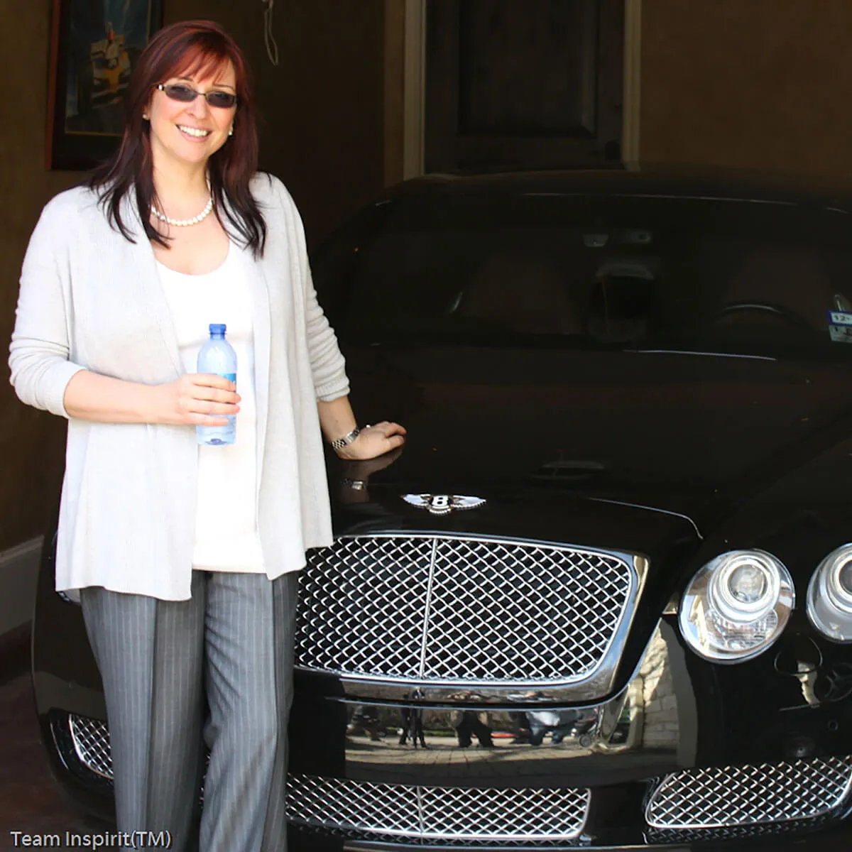 Smiling woman in white cardigan standing next to black Bentley car