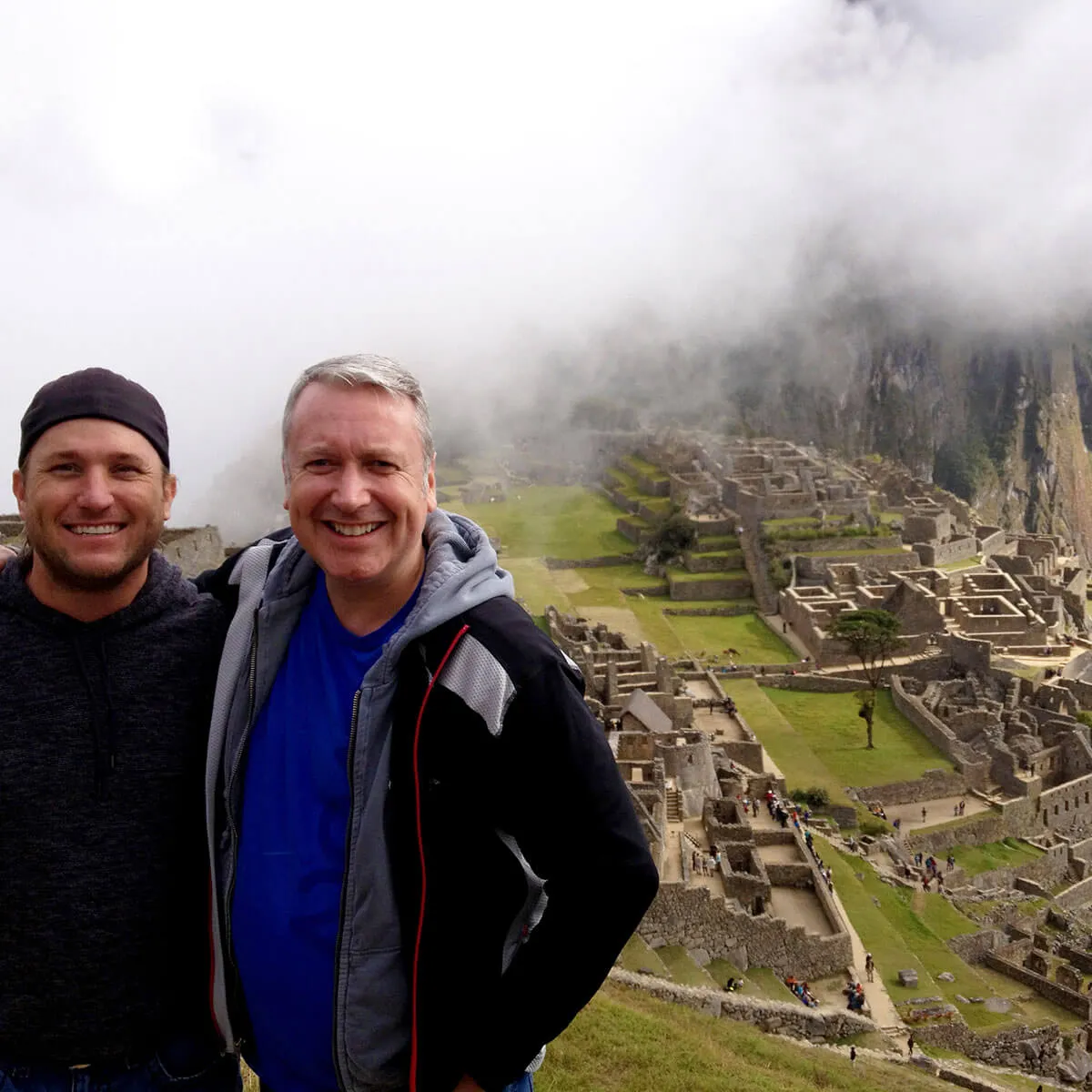 Two travelers smiling at Machu Picchu with misty mountains in background