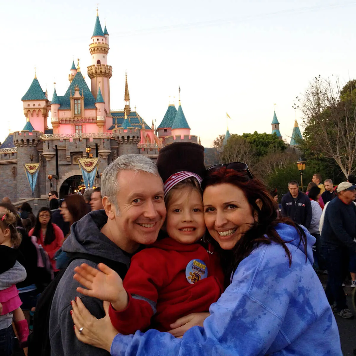 Family smiling together in front of Disneyland's iconic pink and blue castle