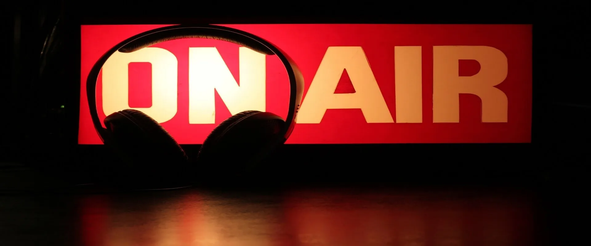 Headphones in front of glowing red On Air radio broadcast sign