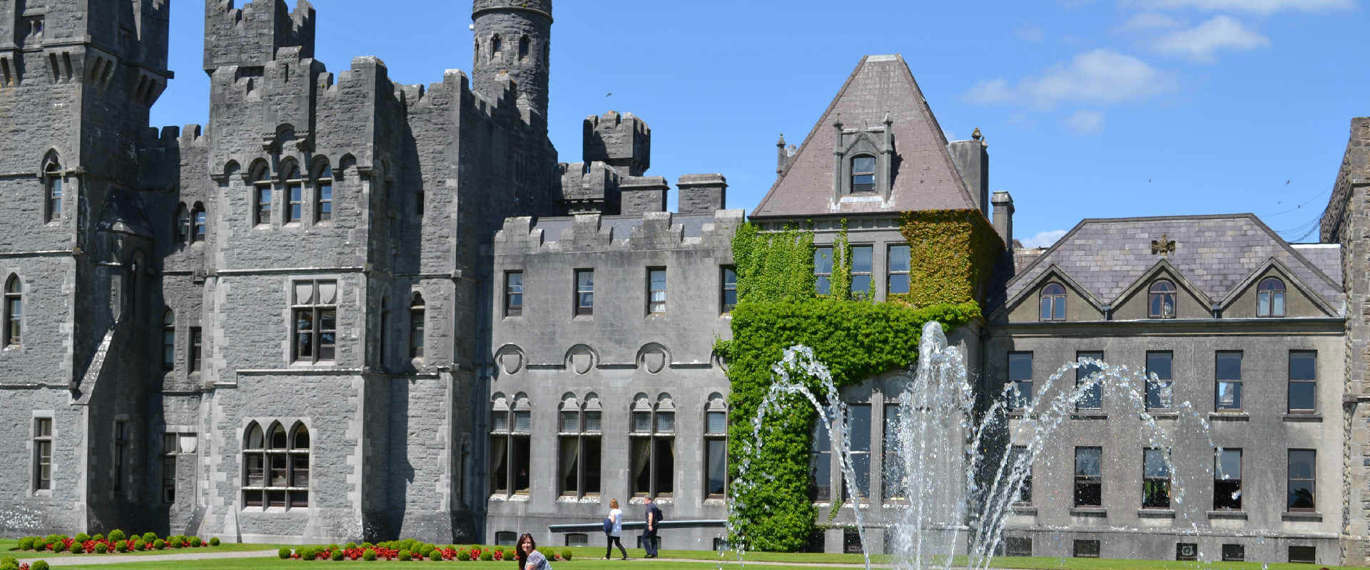 Historic Irish castle with stone walls, towers, and fountains on green lawn