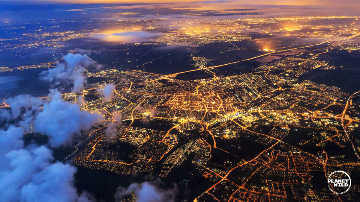Aerial night view of a city spread out below, lights glowing through scattered clouds.