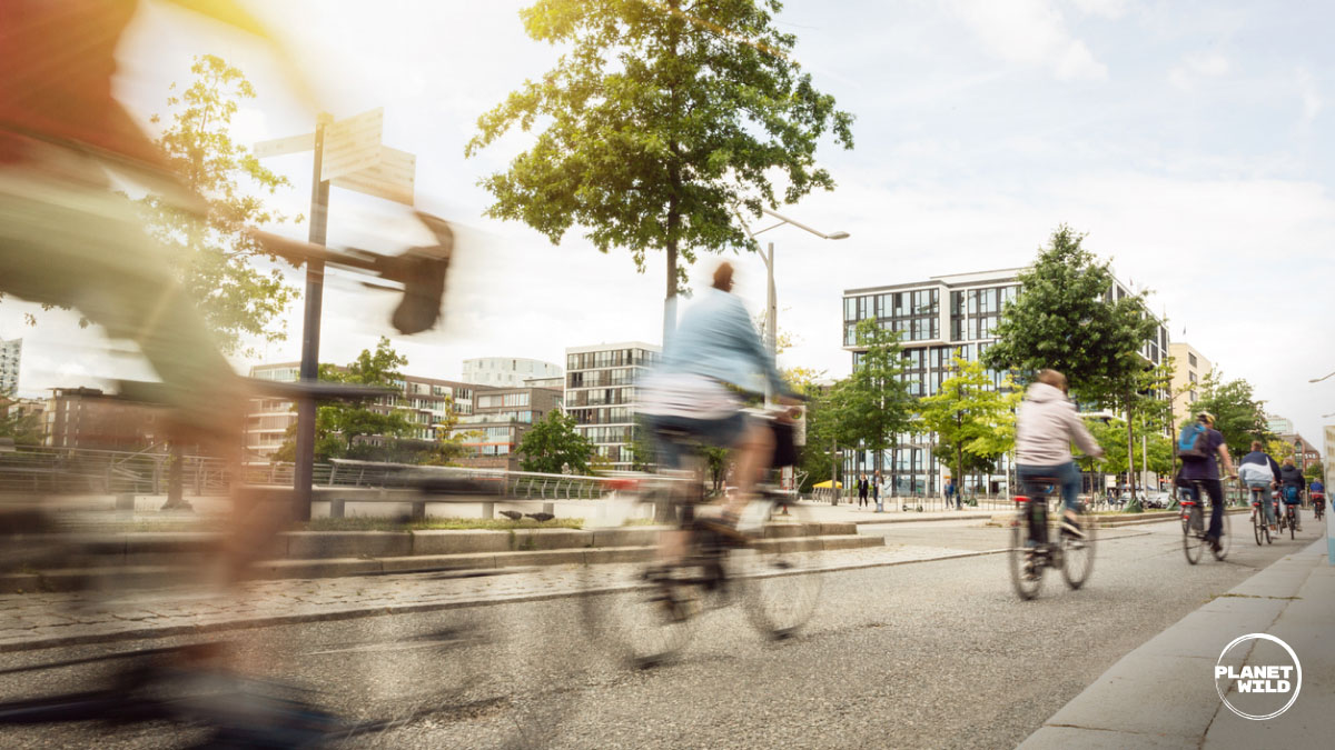 Blurred cyclists riding along a city street lined with modern apartment buildings.