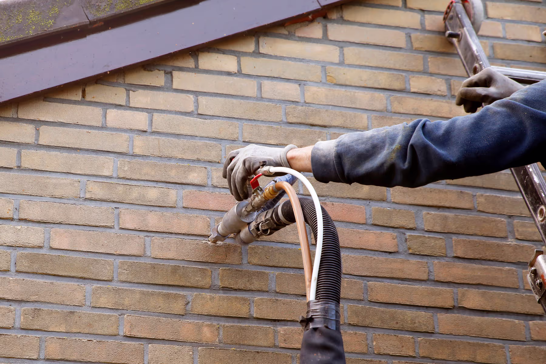 Een persoon in een shirt met lange mouwen gebruikt een gereedschap om kabels tegen een bakstenen muur door te knippen of te verwijderen. De afbeelding legt alleen de arm en een deel van het lichaam van de persoon vast, met de focus op de actie die op de kabels wordt uitgevoerd.