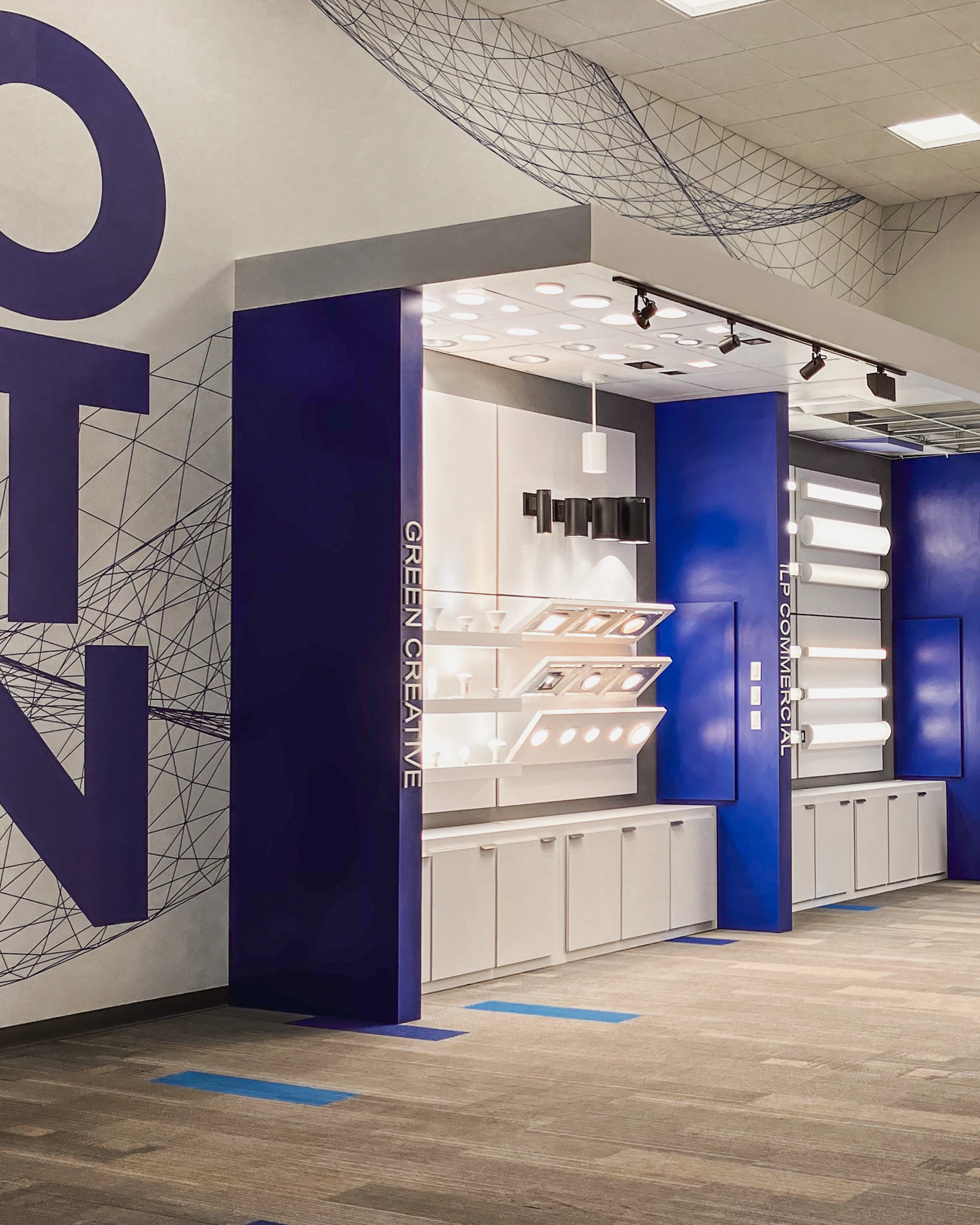 Illumus showroom showing section of the display for their product.  White with blue divider walls.  Full coverage wall graphics.