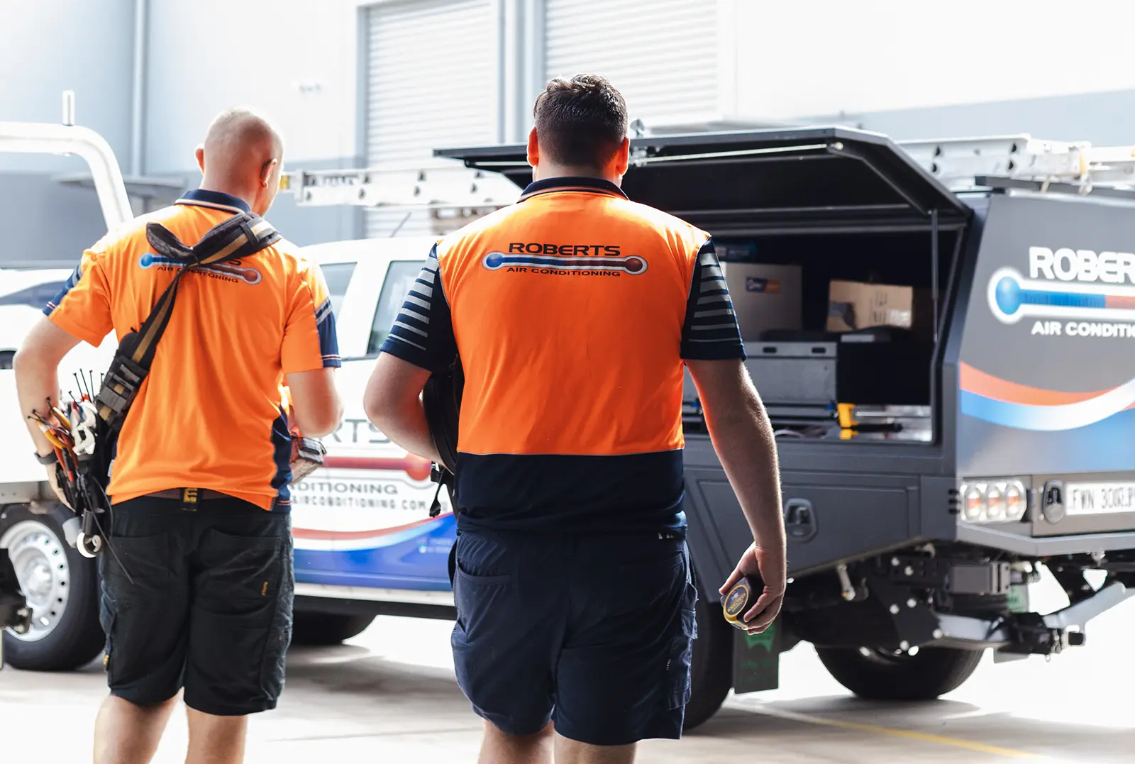 Two tradesmen walking toward a vehicle holding tools.