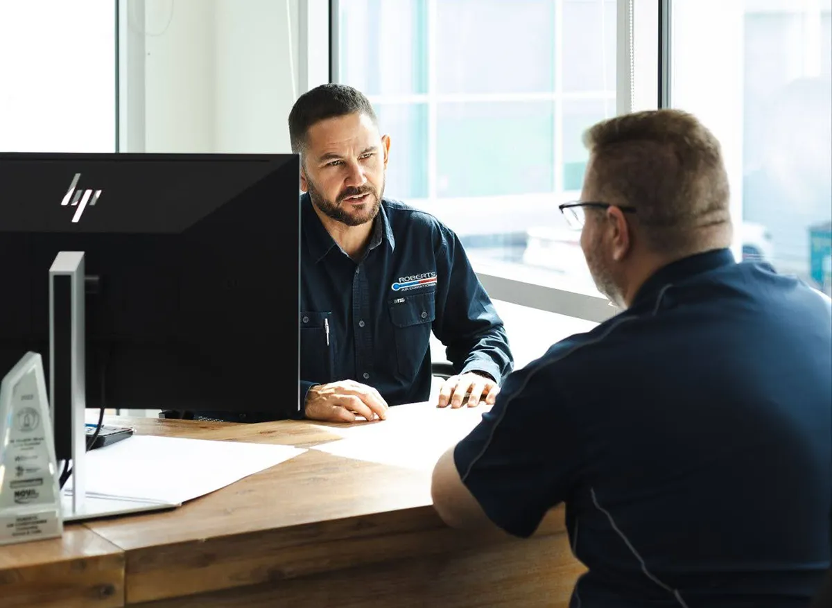 two businessmen sitting at a desk and talking in an office
