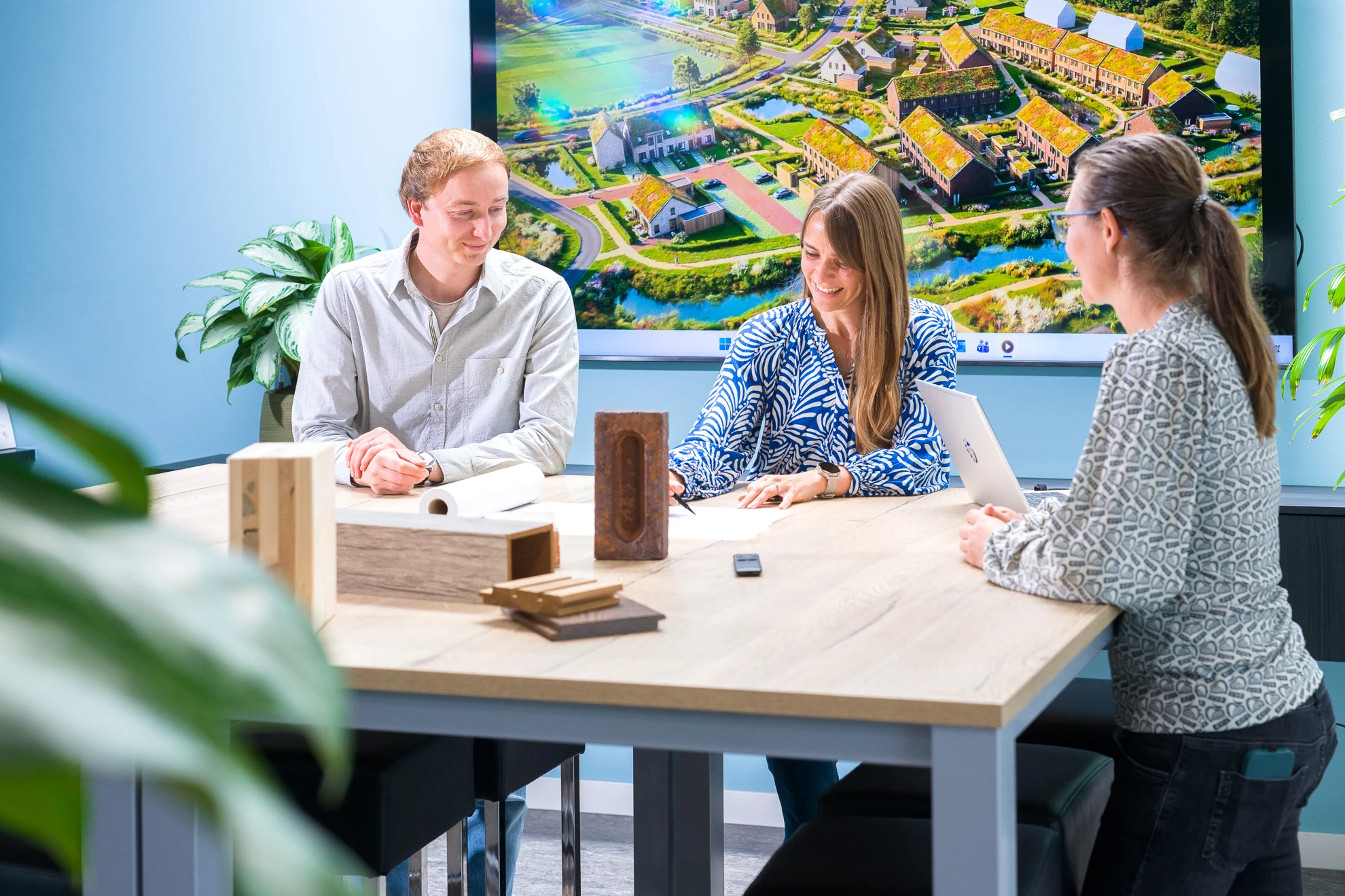 Drie medewerkers van Archifit bespreken een ontwerp met bouwtekeningen en materiaalmonsters op tafel.