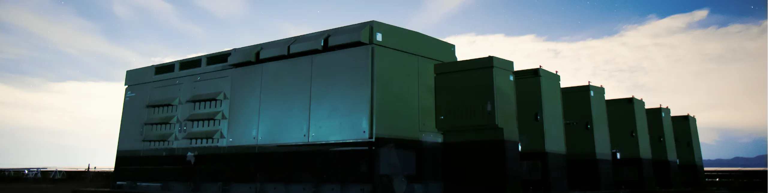 Large power conversion systems for energy storage lined up outdoors beneath a blue sky at dusk.