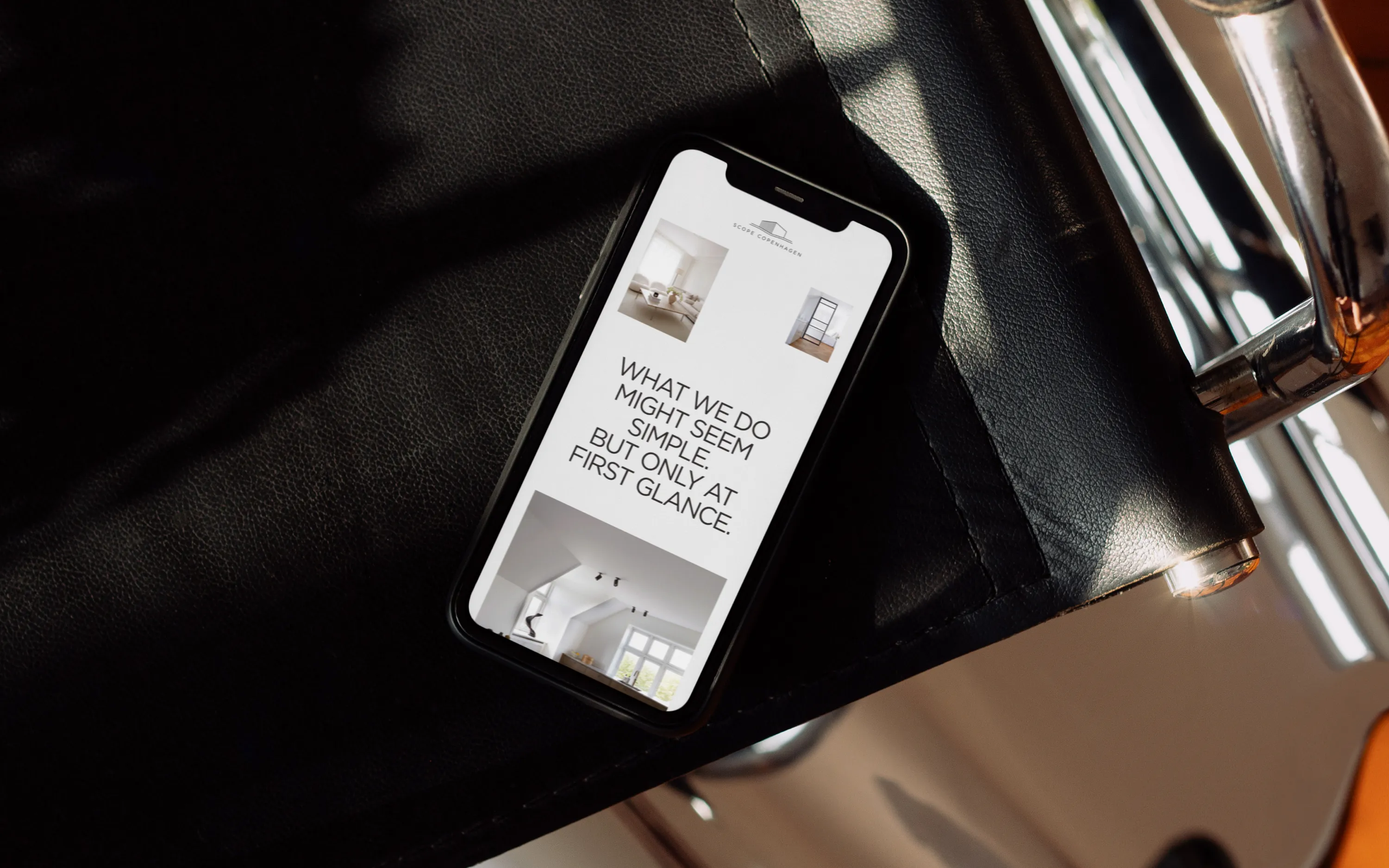 Smartphone on black leather armchair showing a website with text and interior photos.