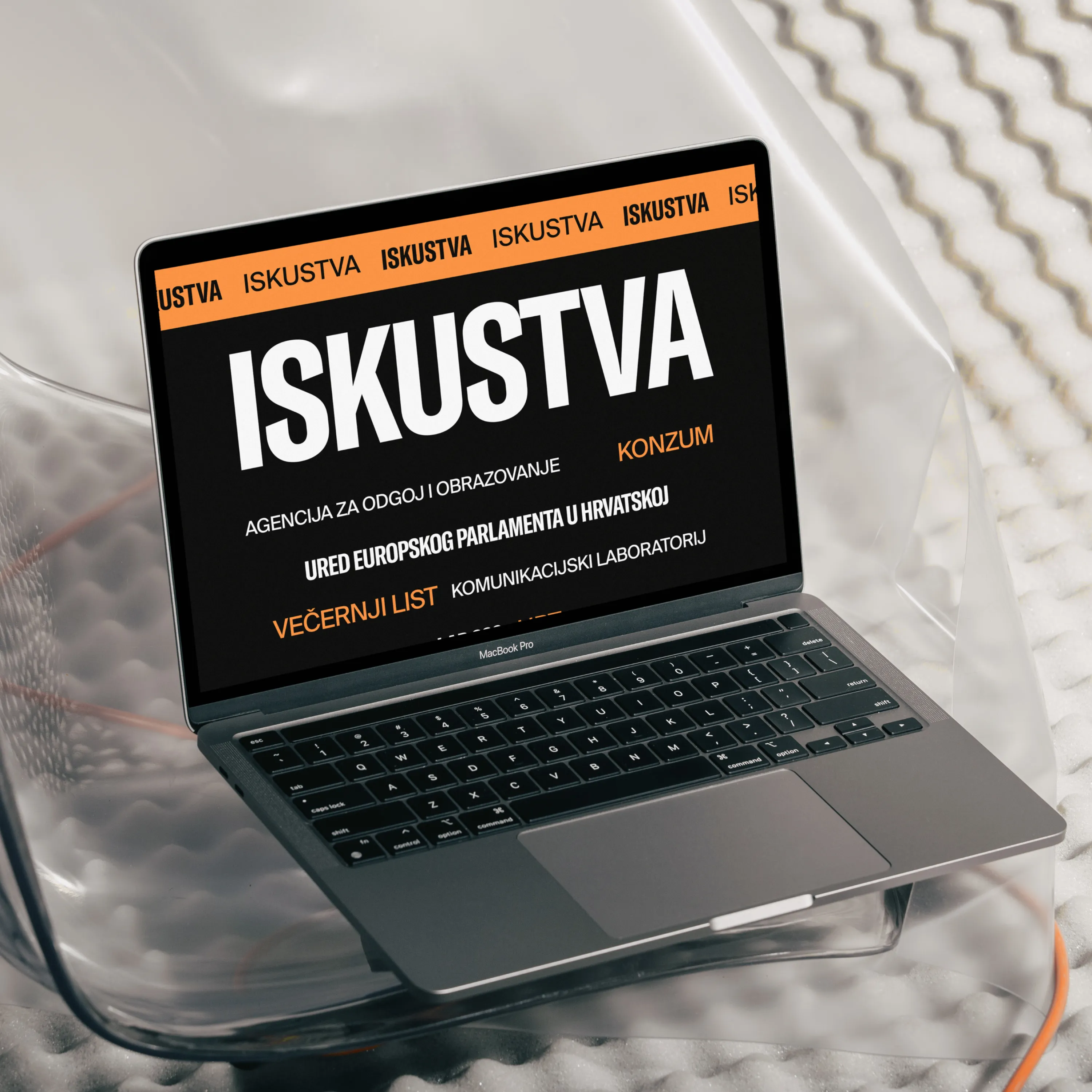 MacBook Pro on transparent chair displays 'ISKUSTVA' and related text in Croatian on screen.