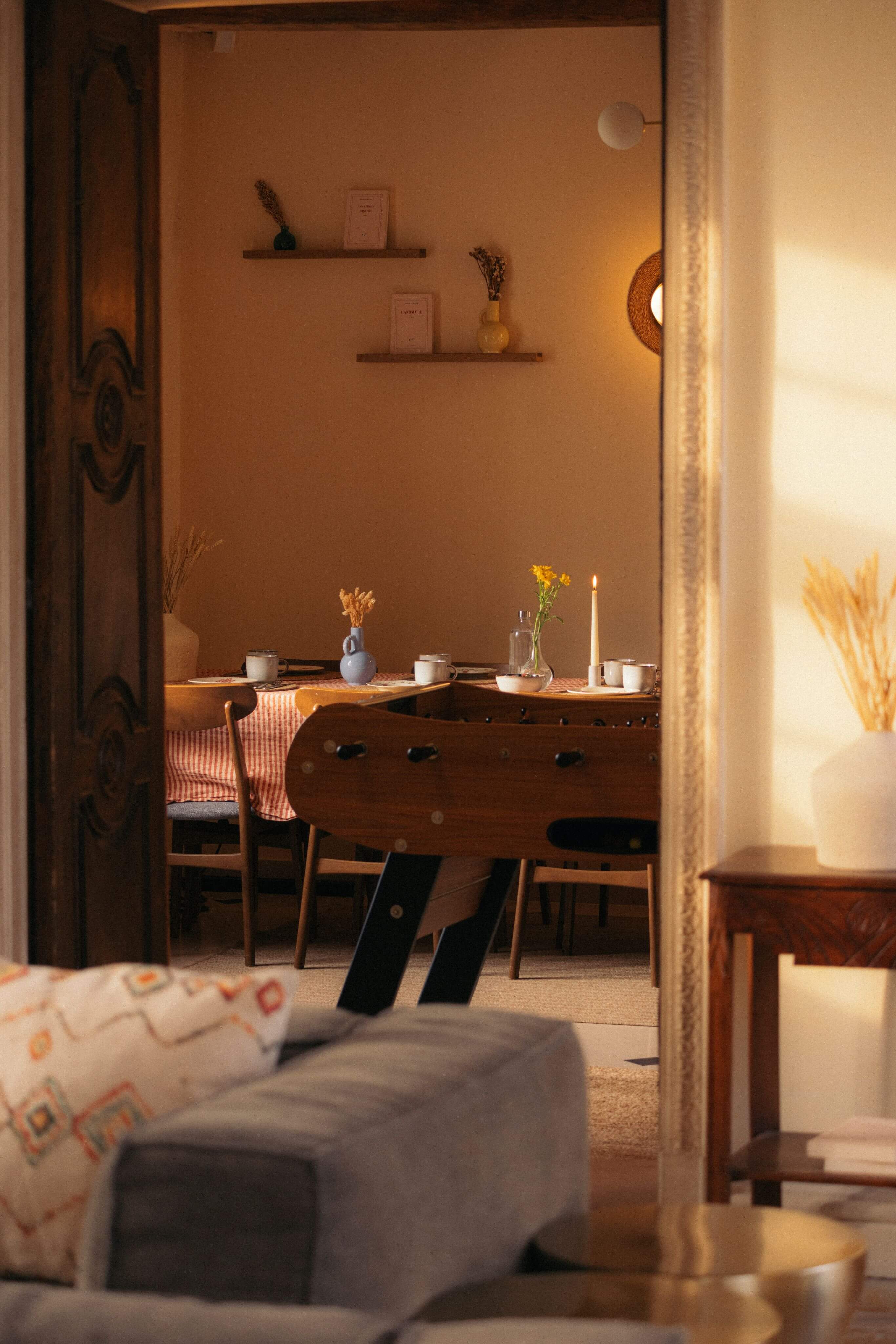 Salle à manger chaleureuse vue à travers une porte avec table, chaises, bougie allumée et décorations.