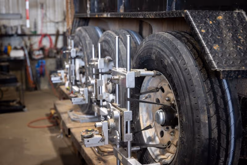 Heavy-duty truck undergoing precise multi-axle wheel alignment in a repair shop, with specialized alignment tools attached to each wheel.