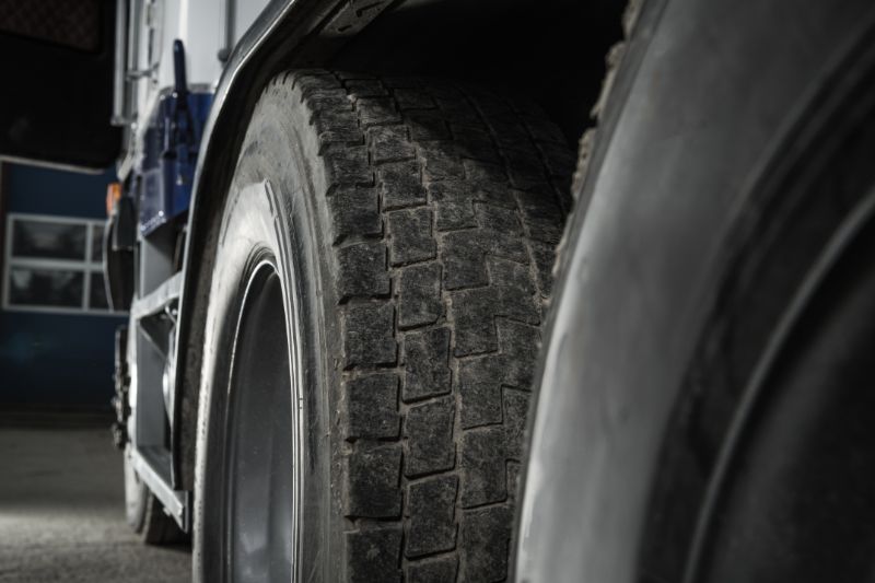 Close-up of a semi-truck tire showing detailed tread pattern, sidewall, and wheel rim, emphasizing durability, traction, and inspection for maintenance.
