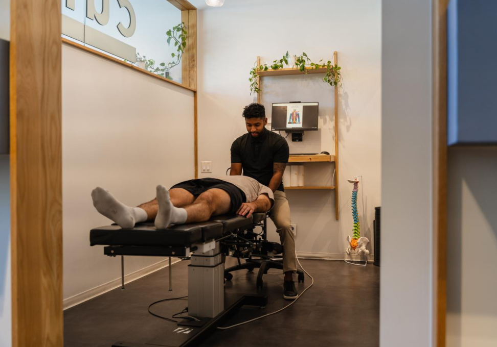 A Calgary chiropractor performing a gentle adjustment on a male patient lying on his back during a treatment session. 