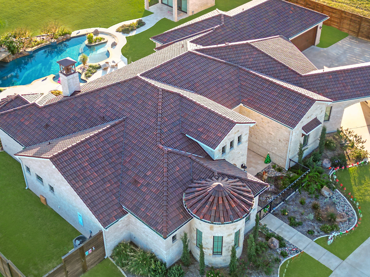 Aerial view of a large house with a tiled roof, turret, landscaped garden, and a curvy pool with rock features in the backyard.