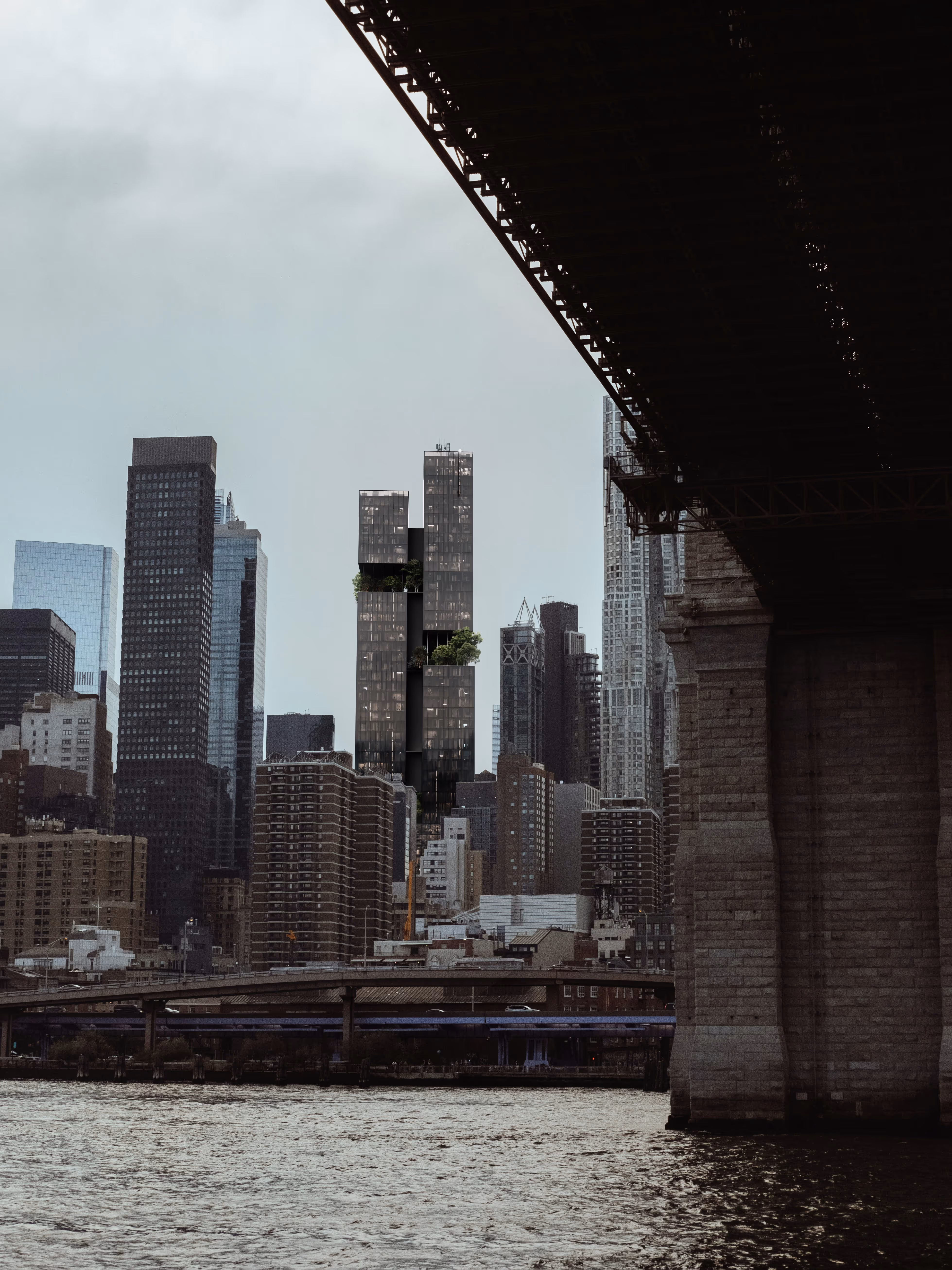 Photorealistic render of a modern skyscraper concept in New York City, viewed from under a bridge, showcasing green terraces integrated into the building's sleek, glass design.