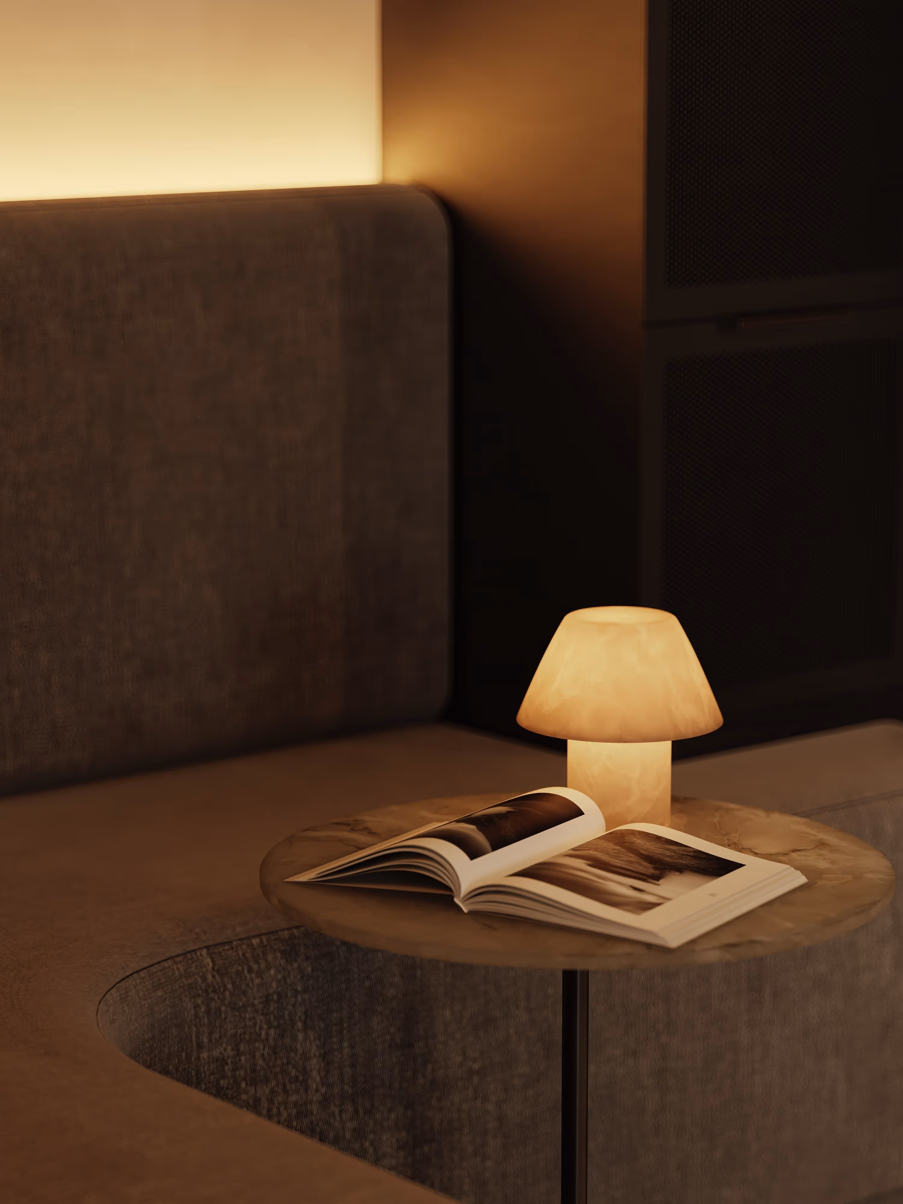 A close-up of a lounge table with a small lamp and an open book. The intimate lighting and curved seating create a cozy, reflective mood within the office's relaxation area.