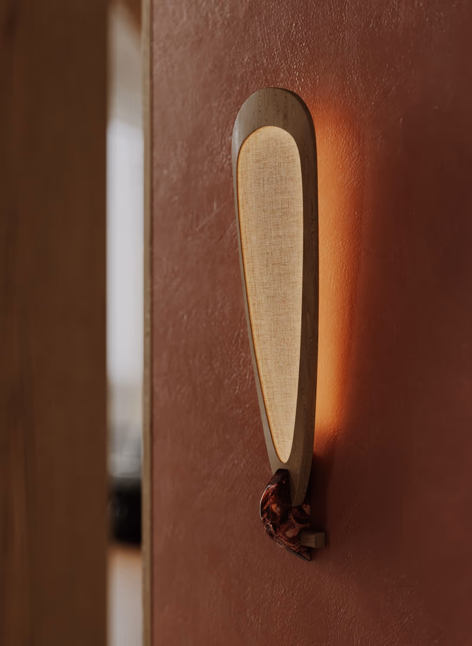 Close-up view of a minimalist wall sconce with a fabric shade, mounted on a warm brown wall, blending with the textured surface for a soft lighting effect.