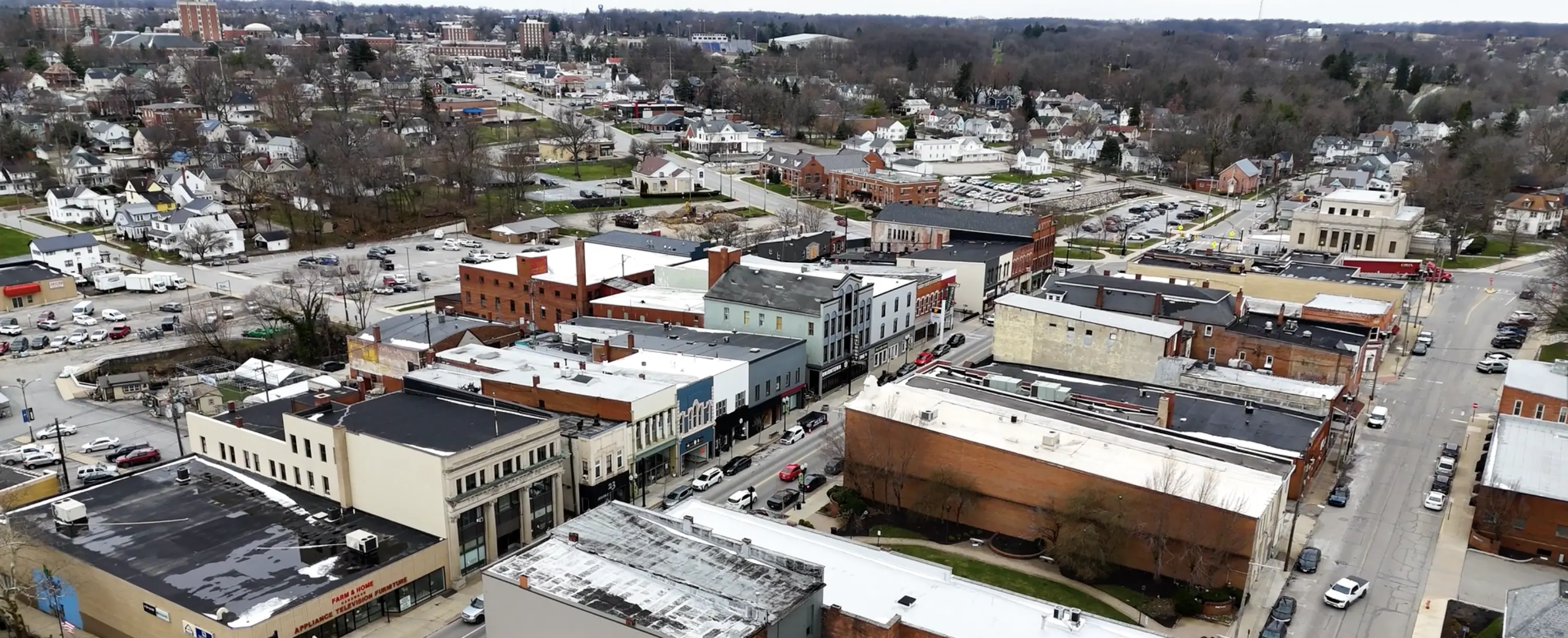 Aerial view of a small town with downtown buildings, streets with cars, residential houses, and trees without leaves in early spring or late fall.