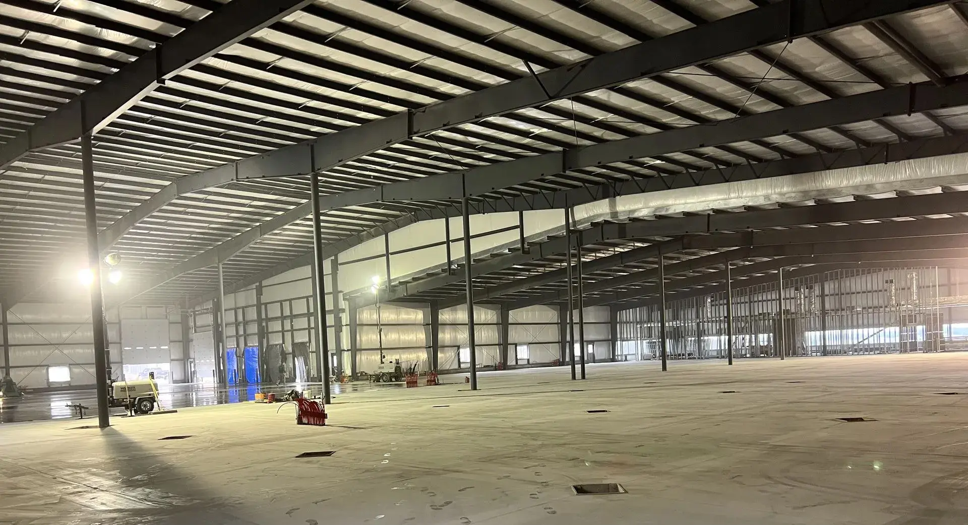 Interior view of a large commercial building under construction with concrete flooring and steel beam framework.
