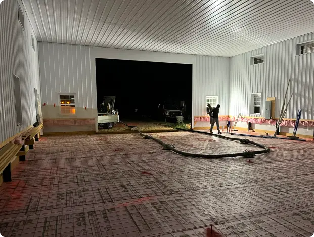 Indoor industrial space under construction with a grid-patterned surface and two workers handling large hoses.